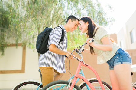 Happy loving couple in love touching their foreheads and smiling about to kiss while going on a date on a bike rideの写真素材