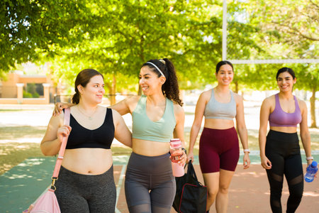 Female best friends with diverse bodies hugging and laughing while having fun working out outdoors...