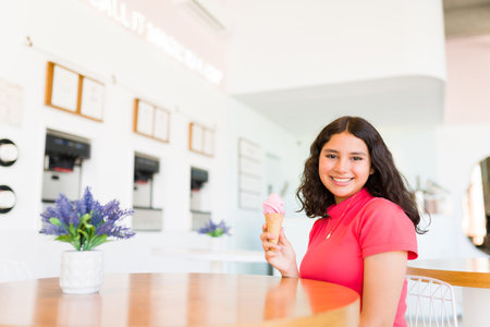 Adorable hispanic girl making eye contact while buying and enjoying eating a delicious ice cream cone for a sweet dessertの写真素材