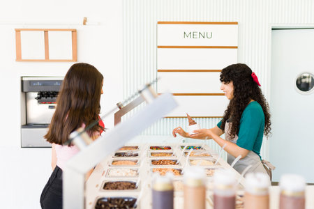 Side view of woman worker putting toppings on the ice cream or frozen yogurt for teen customers buying in the gelato shopの写真素材
