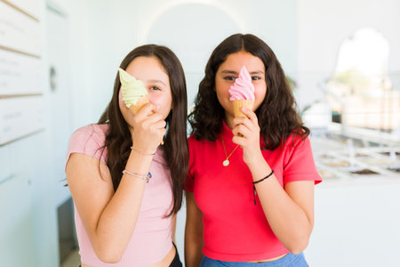 Funny teen girls friends enjoying eating a delicious ice cream cone together and buying sweet treats...