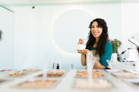 Beautiful happy woman worker smiling looking at the camera while eating delicious frozen yogurt or...