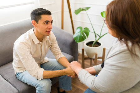 Sad caucasian man holding hands with his professional therapist while asking for help and advice for his depressionの写真素材
