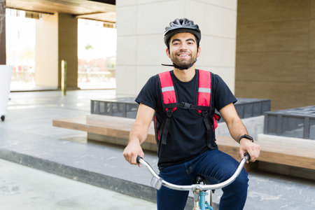 Happy food delivery worker smiling making eye contact looking cheerful while riding his bicycle working running errandsの写真素材