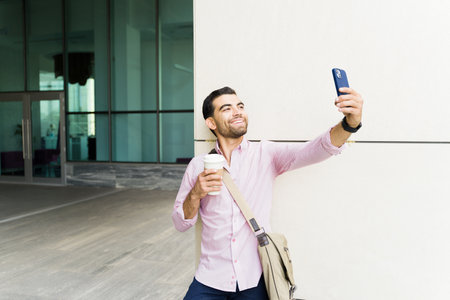 Excited casual businessman taking a selfie with his phone for social media while drinking coffee and...
