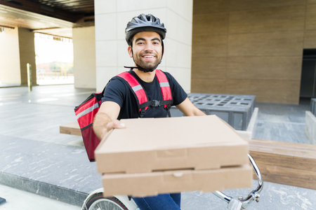 Happy latin man delivering pizza and while working for a food delivery app riding a bike and smilingの写真素材
