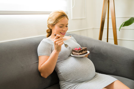 Attractive woman enjoying her pregnancy and eating a big and delicious slice of cake as one of her cravingsの写真素材