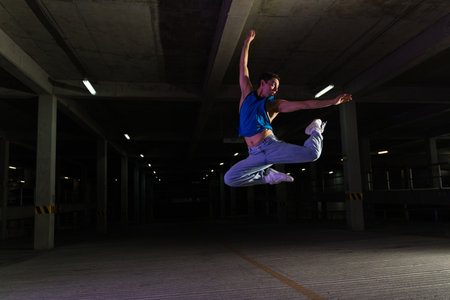 Hispanic male street dancer looking happy and artistic dancing to funky cool music in a dark parking garageの写真素材