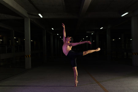 Attractive latin male dancer dancing at night in a dark parking lot and doing an arabesque classic ballet poseの写真素材