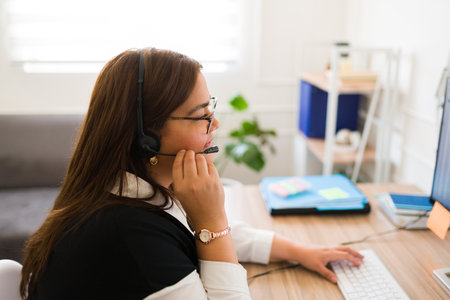 Overweight hispanic woman working in customer support service while talking with a headset sitting...