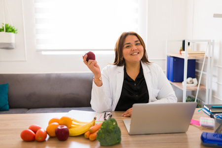 Portrait of a happy fat woman nutritionist smiling in her office and  holding an apple while talking about a healthy dietの写真素材