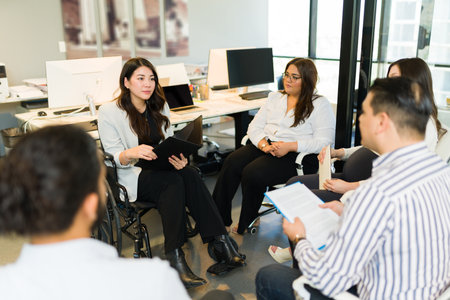 Hispanic businesswoman with disability sitting on a wheelchair talking over new business strategy...