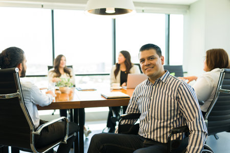 Happy mid adult disabled businessman sitting on a wheelchair making eye contact during meeting with...