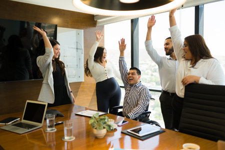 Cheerful multiethnic business professionals raising hands to celebrate in office boardroom
