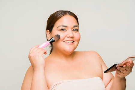 Gorgeous large woman smiling and getting ready while putting on makeup using a brush with a lot of self confidenceの写真素材