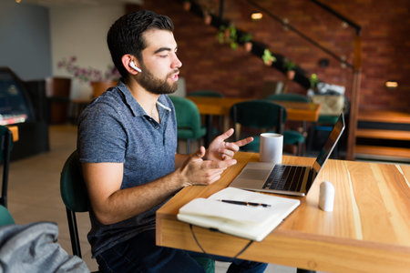 Handsome man and freelance talking during a video call using his laptop and doing remote work at the...