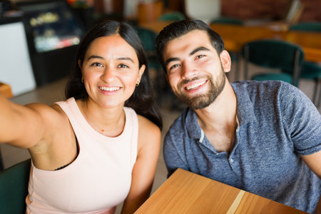 Personal perspective of an attractive latin couple smiling taking a selfie and looking happy during a romantic dateの写真素材