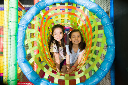 Portrait of cute little girl friends smiling and looking happy while playing in the playground tunnel and having funの写真素材