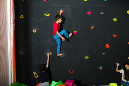 Latin kid boy rock climbing in the indoor play area while playing with a group of children and having funの写真素材