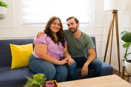 Portrait of a beautiful romantic couple hugging and smiling while relaxing together in the living room home during a dateの写真素材