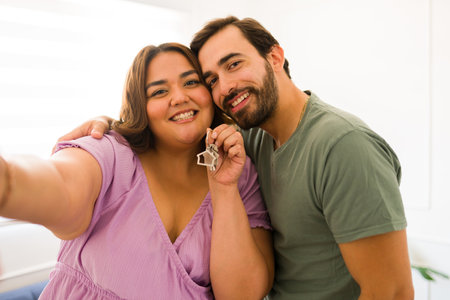 Cheerful couple holding their new house keys after buying a home or moving in together smiling looking happyの写真素材