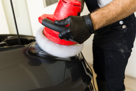 Close-up of a male worker using orbital polisher for polishing car headlight at auto detailing...