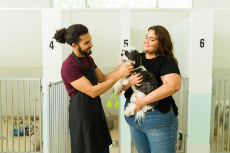 Cheerful workers carrying and petting an adorable shih tzu dog while looking happy at the pet hotel or dog daycareの写真素材