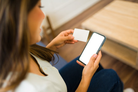 Happy woman seen from behind doing online shopping paying with a credit card looking at her smartphone mock up blank screenの写真素材