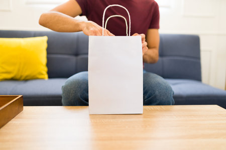Young latin man in the living room with a small blank mockup shopping bag with copy spaceの写真素材