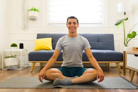 Attractive young man doing yoga at home wearing a fitness gray t-shirt for a workoutの写真素材
