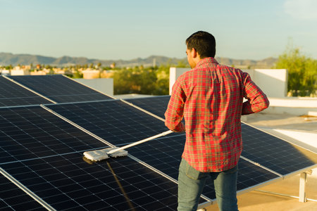 Young man and home owner cleaning the solar panels on the rooftop while using clean energy