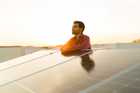 Relaxed latin man and home owner at the rooftop looking happy about using solar panels and clean sustainable energyの写真素材