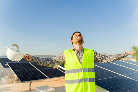 Excited man engineer with a safety vest and helmet celebrating finishing the installation of solar panels and photovoltaic cellsの写真素材