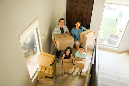 High angle of a happy family with children smiling and carrying a lot of boxes to unpack while moving into a new house or apartmentの写真素材