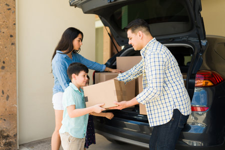Kid helping his parents carrying cardboard boxes from the car while moving into a new house or rental apartmentの写真素材