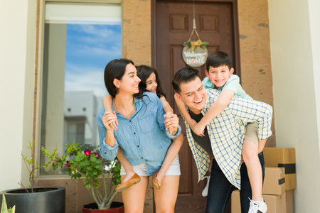 Excited family with children piggybacking having fun moving into a new home together playing in the house entrywayの写真素材