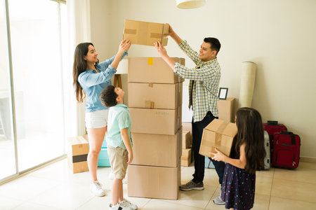 Full length of a fun happy family playing with cardboard boxes while unpacking and moving into a new house feeling cheerfulの写真素材