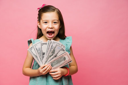 Happy little girl with a toothless smile looking excited and surprised feeling rich getting her allowance money giftの写真素材