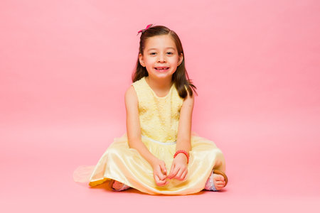 Relaxed elementary age little girl sitting and relaxing wearing a summer dress showing her toothless smile looking happyの写真素材