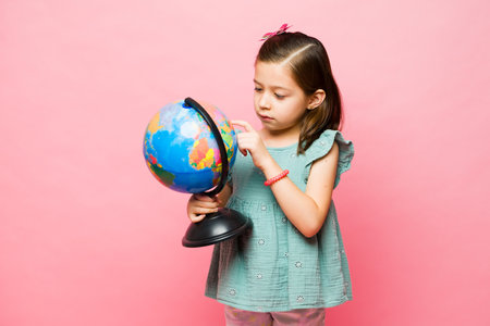 Adorable elementary age little kid looking up a country while learning geography education using a globe in schoolの写真素材