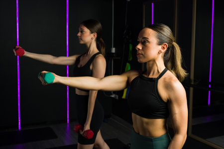 Attractive fitness women lifting dumbbell weights and working out together during a functional training classの写真素材