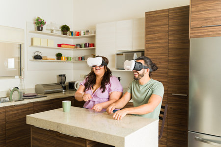 Cheerful latin couple in the kitchen relaxing and having fun together using virtual reality VR...