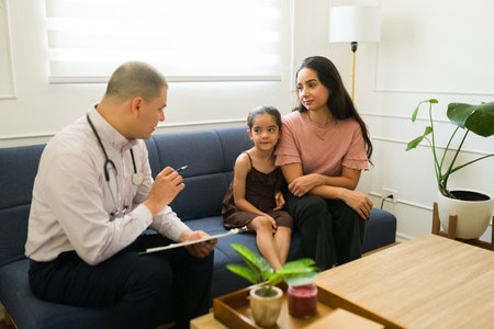 Mom talking to the pediatrician about her sick 6 year old kid's health while having a doctor's visit in the living roomの写真素材