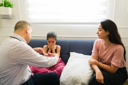 Sick little girl covering her mouth and rejecting the cough syrup medicine from the pediatrician during a doctor's visitの写真素材