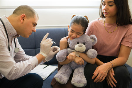 Scared kid feeling sick hugging her teddy bear while looking afraid of a vaccine injection during a medical doctor's visitの写真素材
