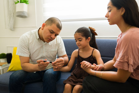 Mexican father using a glucometer monitor at home to check blood sugar levels of her sick little kid with diabetesの写真素材