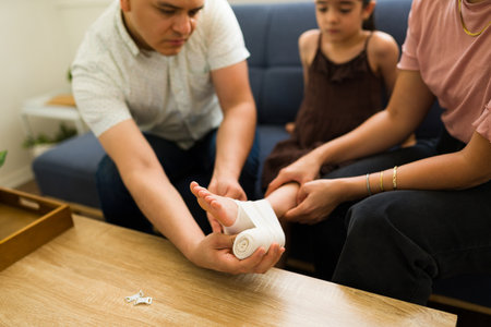 Close up of a family in the living room putting a bandage on the foot of their injured little kid in pain after an accidentの写真素材