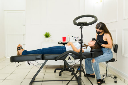 Cosmetologist with a face mask working on a microblading service and eyebrow design with a young...