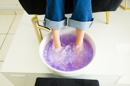 Close up of a young latin woman soaking her feet in gel salts for exfoliating her feet during a relaxing pedicure serviceの写真素材