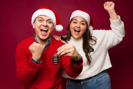 Happy hispanic couple looking excited and celebrating buying a new car during the christmas holidaysの写真素材